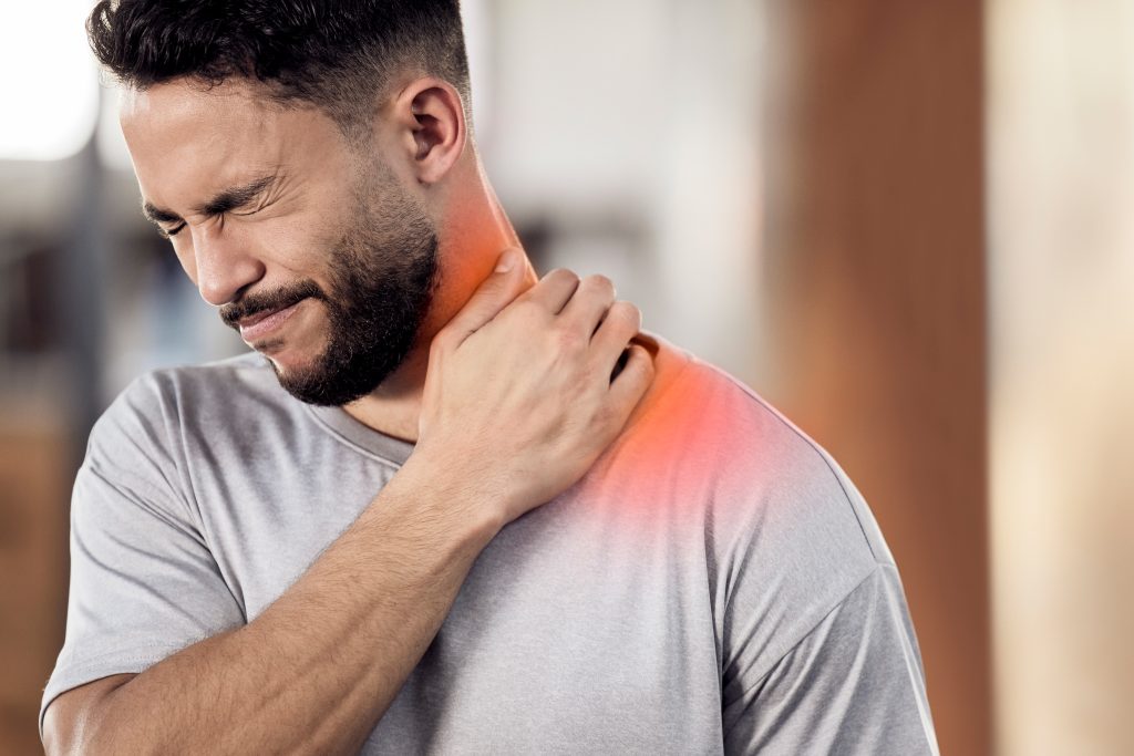 A man in a gray shirt holds his neck and appears to be in pain, with a red highlight indicating discomfort or injury in the neck area.